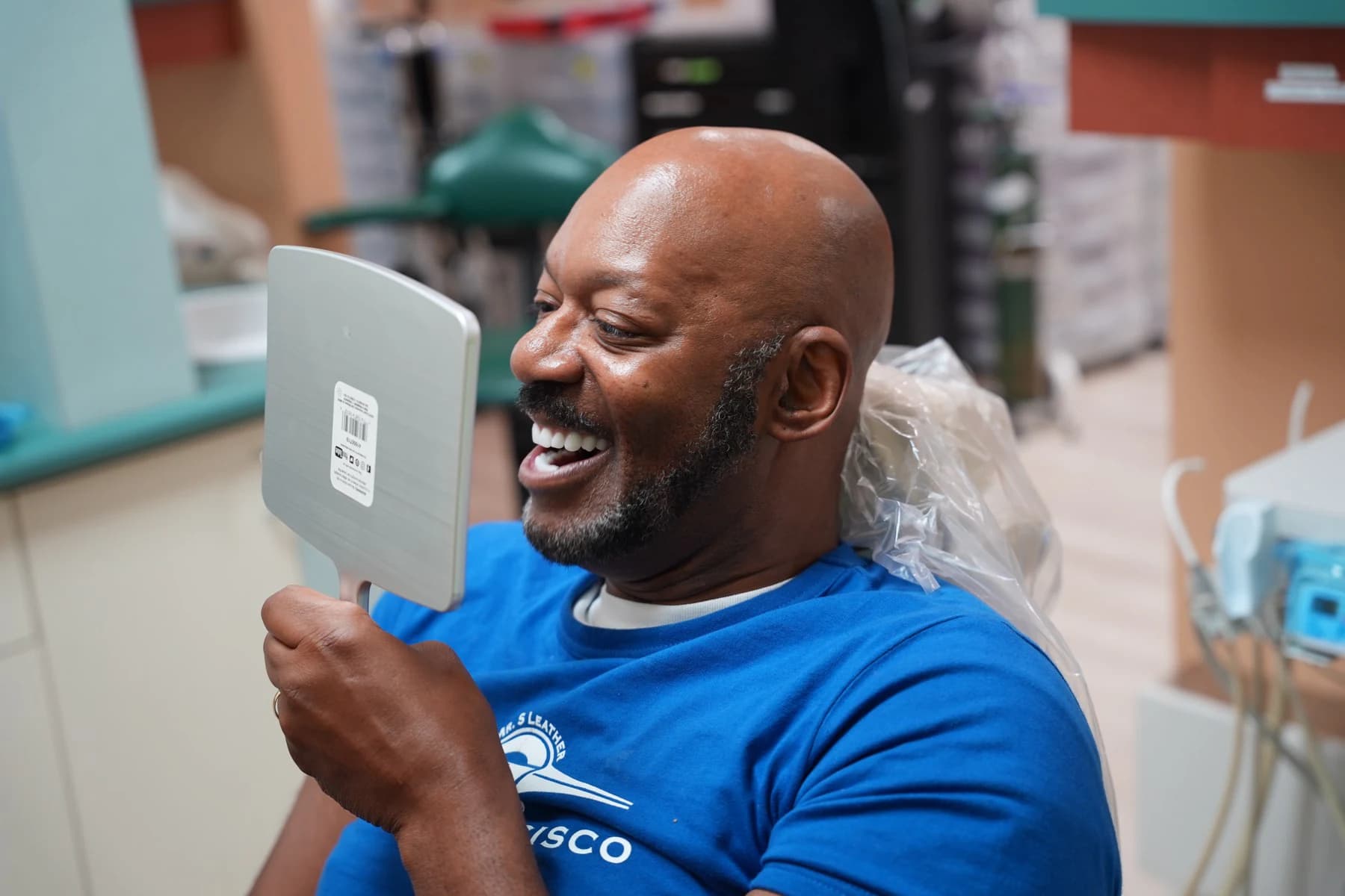 A patient laughing at his new smile in a hand mirror