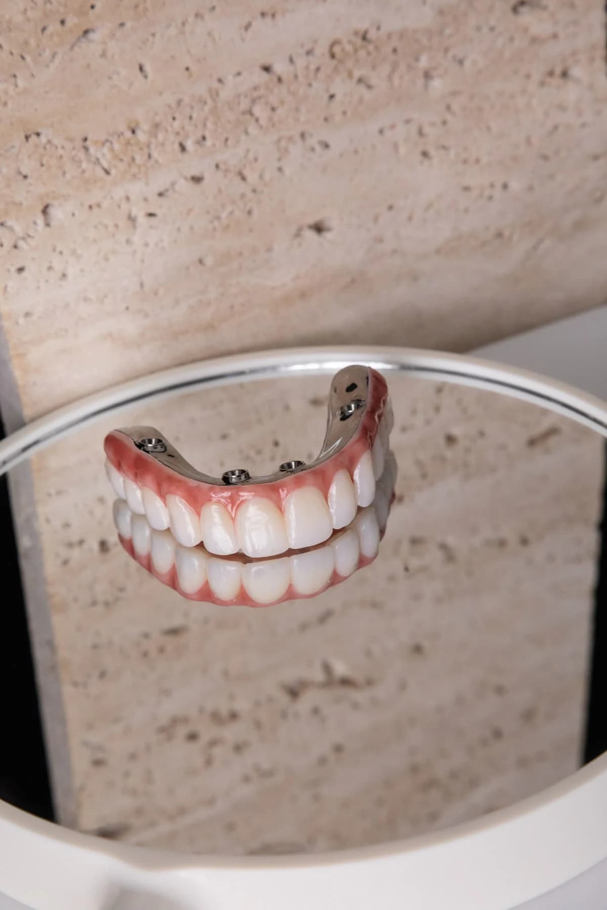 Finished zirconia full-arch prosthesis reflected on a dark surface