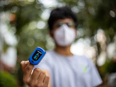 A masked person using a pulse oxymeter